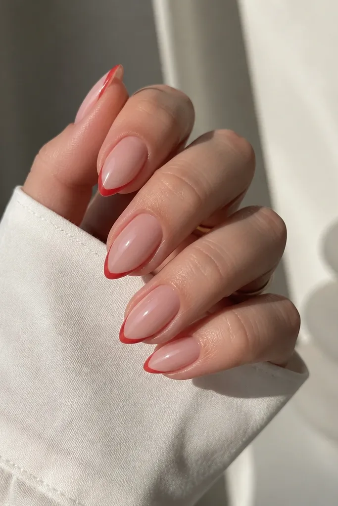 Short stiletto nails with a sheer pink base and a very thin French line. The French line is true red and follows the stiletto curve cleanly, with a glossy top coat.