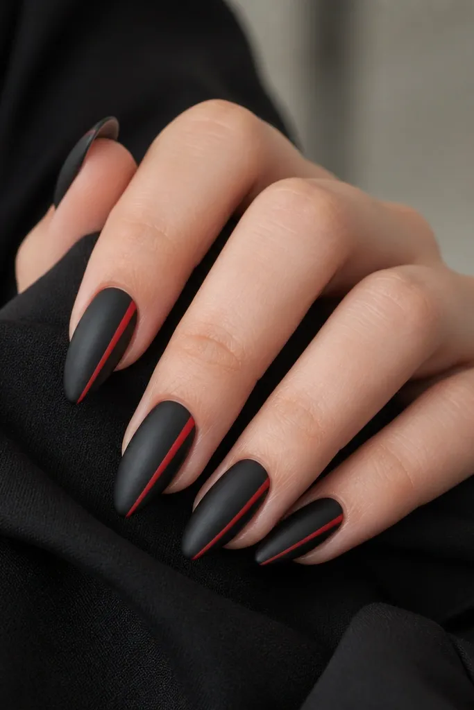 Short stiletto nails with a dark black satin finish. Each nail has a single thin red stripe running down the side edge from near the cuticle to the tip, sharp and straight.