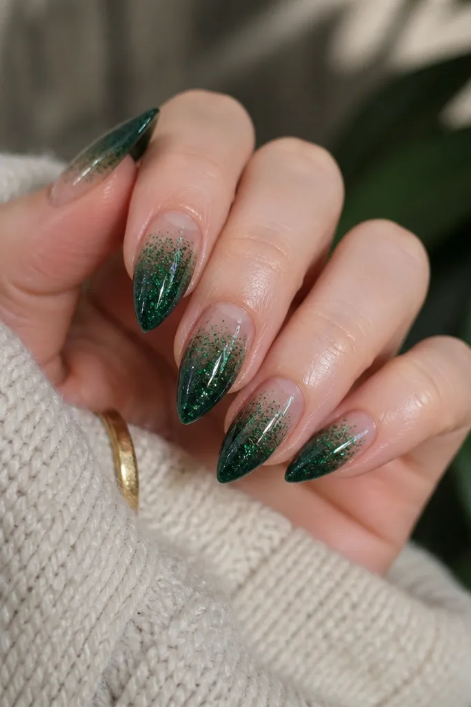 Short stiletto nails with a deep emerald base. The glitter is heaviest at the tips and fades to clear near the cuticle, with a smooth glossy top coat.