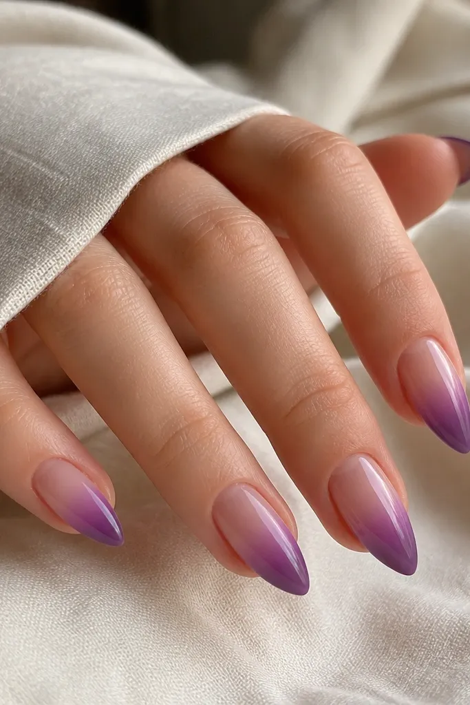 Short stiletto nails with a sheer nude base fading into grape purple toward the tips. The gradient looks smooth and glossy with clean sidewalls.