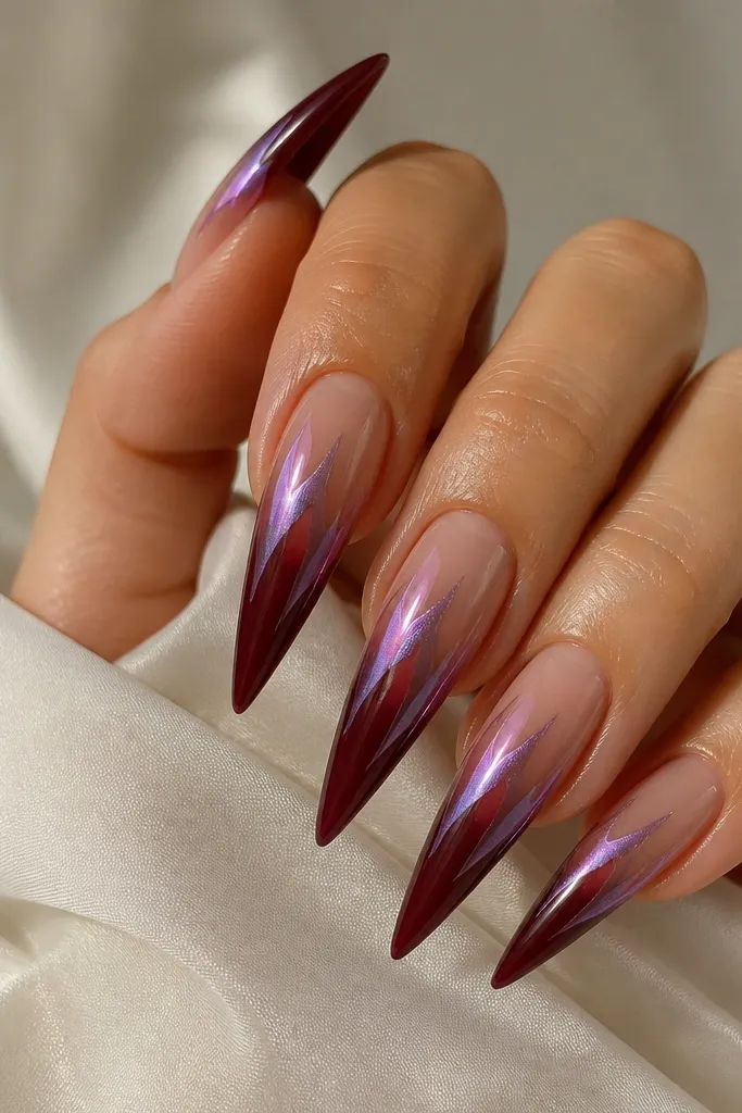 Long stiletto nails with nude at the cuticle blending into deep burgundy at the tip. Violet chrome is applied as small flicks on the upper half, leaving gaps for the ombre to show.