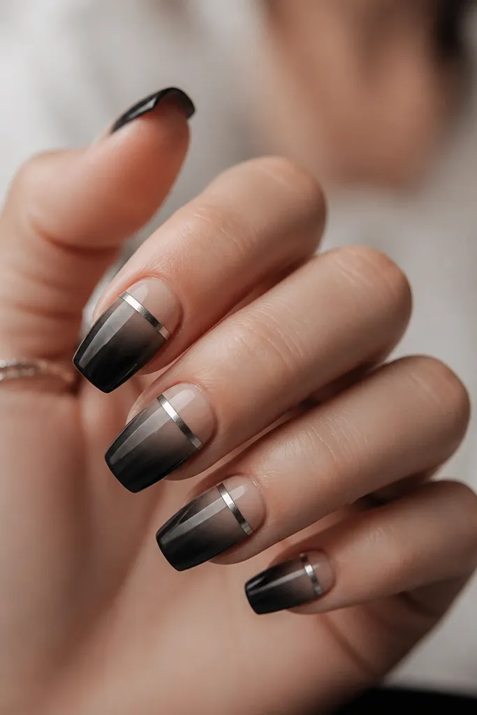 Short coffin nails with neutral beige at the cuticle fading into soft black at the tips. A graphite chrome strip runs horizontally across the upper third, with a subtle metallic sheen.