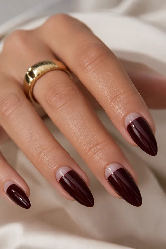 Short stiletto nails in glossy black cherry. On each nail, a soft half-moon of clear gel sits right at the cuticle line, leaving a curved negative space. The rest of the nail is fully filled with color.