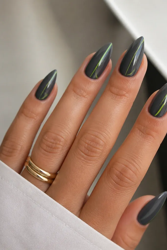 Short stiletto nails in glossy charcoal gray. Each nail has a tiny neon lime line near the sidewall, running from mid-nail toward the tip. The neon line is thin and bright.
