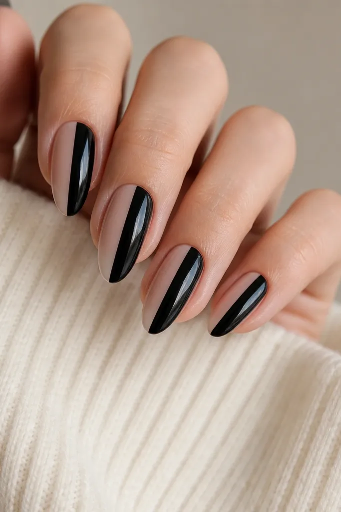 Short stiletto nails divided down the center: left half nude pink and right half glossy black. The center line is sharp and straight from cuticle to tip.