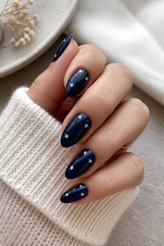 Short stiletto nails painted dark navy glossy. On the tips and upper third, there are tiny white star shapes spaced out evenly. The stars are small and crisp.