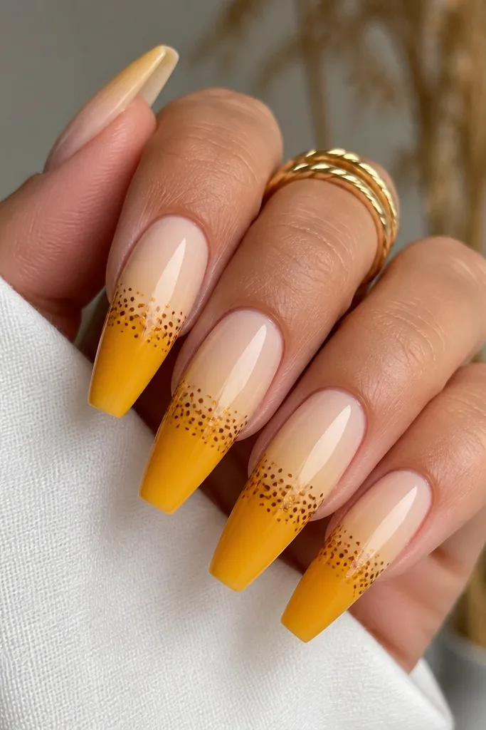 Coffin nails with a yellow ombre that fades from pale at the cuticle to deeper golden at the tip. Brown dots cluster right where the gradient changes, forming a dotted band. Everything looks smooth and glossy.