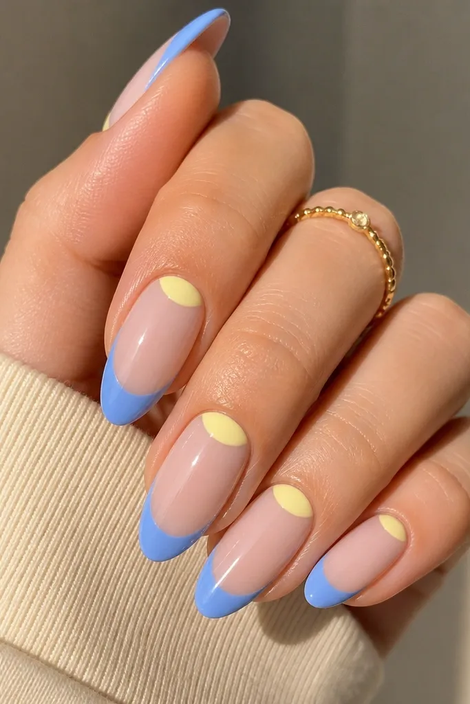 Four nails shown with a soft butter-yellow base on the lower half and periwinkle light blue on the upper tip area, separated by a clean curved half-moon line near the nail bed. Glossy finish, natural nail shape.