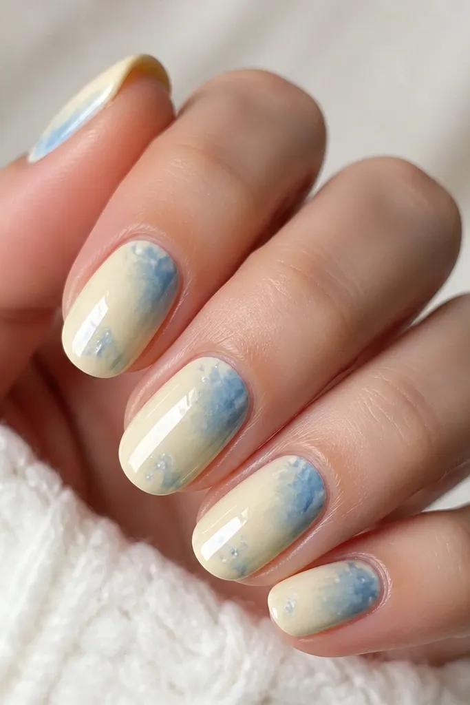 Butter-yellow base with translucent light blue patches and streaks like watercolor, concentrated near the center and fading toward the edges. Glossy top coat.