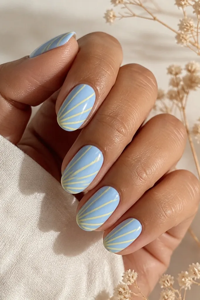 Light blue nails with several thin butter-yellow lines radiating from one side like sunbeams. Lines are straight and evenly spaced. Glossy finish.