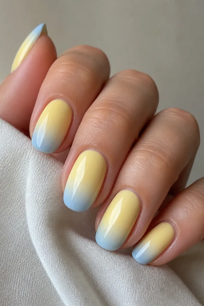Butter-yellow nails with a smooth ombré fade at the tips into light blue, strongest at the edge and fading back toward mid-nail. Glossy.